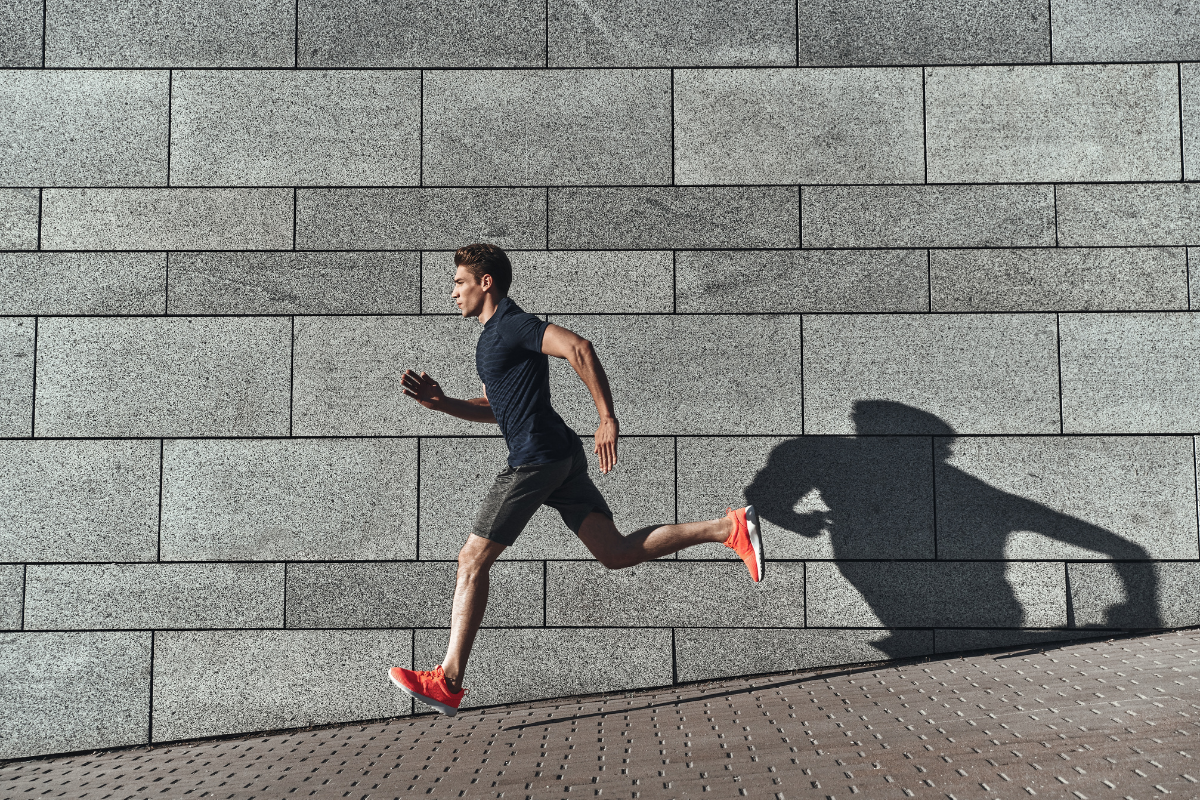 Person running on a sidewalk with a gray brick wall in the background