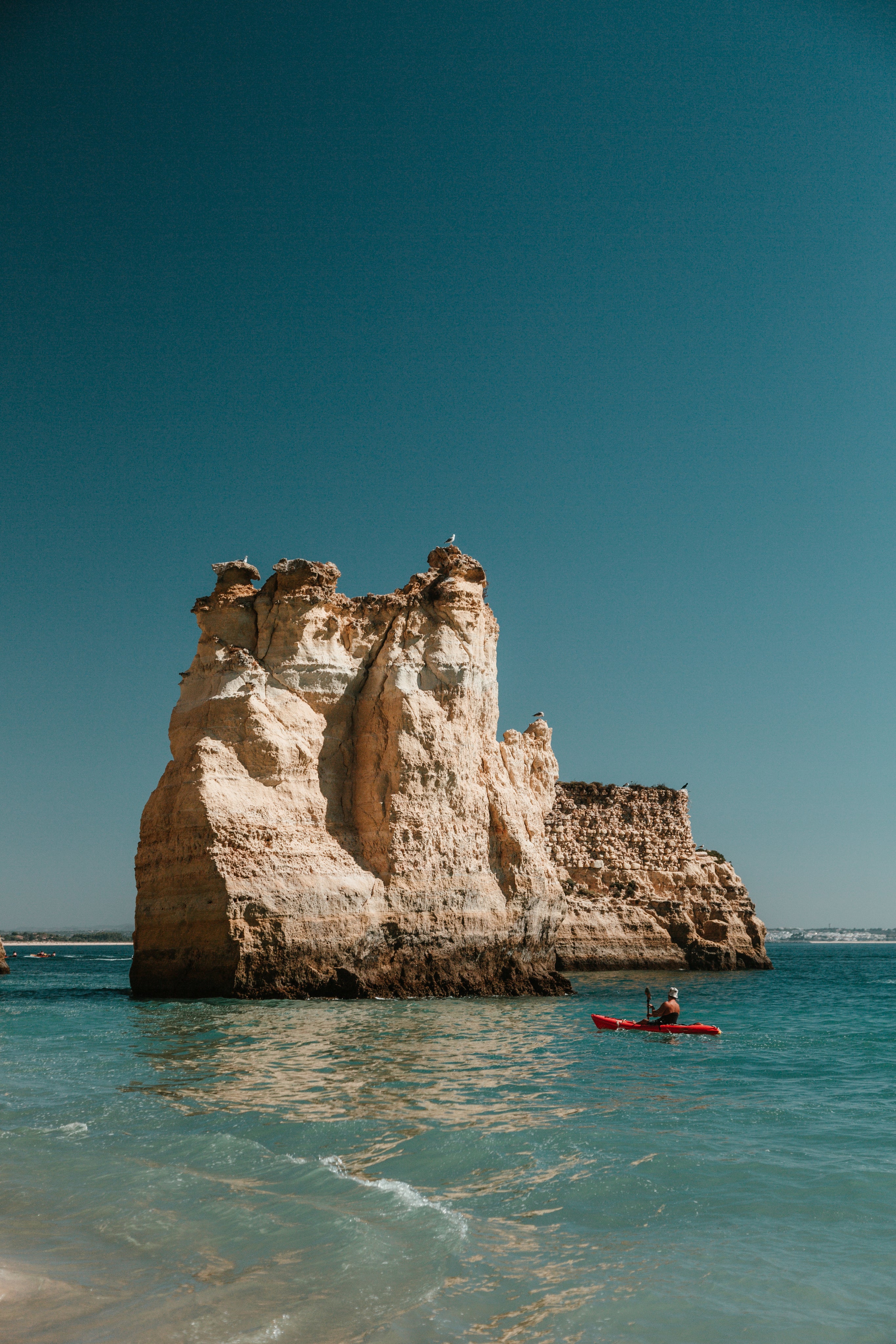 Kayaker paddling beside a limestone sea stack on a calm coastal wellness scene